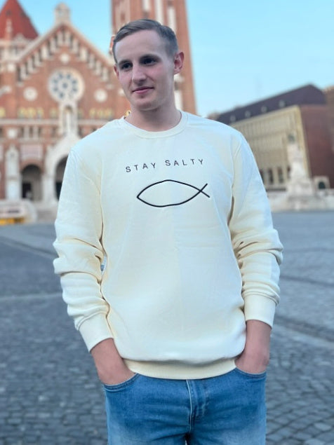 Man wearing the cream Stay Salty embroidered Christian crewneck on Dóm Square in front of the Votive Church in Szeged, Hungary